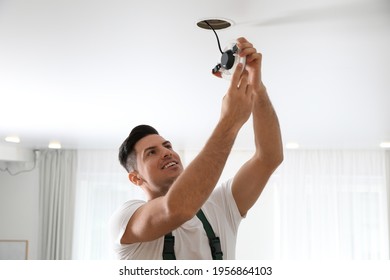 Electrician in uniform repairing lamp on ceiling indoors - Powered by Shutterstock