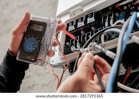 Electrician using a digital multimeter to measure voltage inside an open electrical control panel