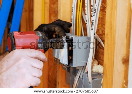 An electrician is using power tool to install circuit breaker in wall of newly built house