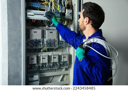 Electrician with wires switching off circuit breakers in fuse box indoors