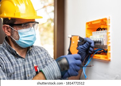 Electrician At Work On An Electrical Panel Protected By Helmet, Safety Goggles And Gloves; Wear The Surgical Mask To Prevent The Spread Of Coronavirus. Construction Industry. Covid-19 Prevention.