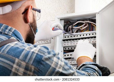 Electrician At Work On An Electrical Panel Protected In Safety Goggles And Gloves; Coronavirus. Construction Industry. Covid 19 Prevention.