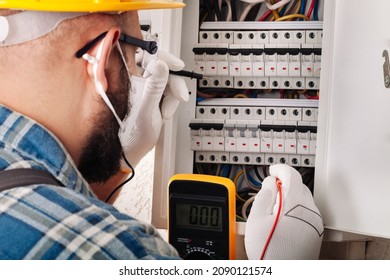 Electrician At Work On An Electrical Panel Protected In Safety Goggles And Gloves; Coronavirus. Construction Industry. Covid 19 Prevention.