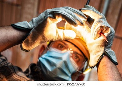 Electrician worker at work replaces the light bulb protected by helmet, safety goggles and gloves. Wear the surgical mask to prevent the spread of Coronavirus. Covid-19 Pandemic Prevention.