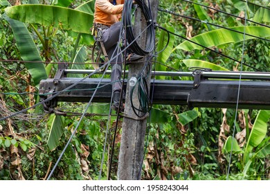 Electrician workers with tools for cutting and connecting wires Climb the electric pole, tilt it, repair the broken wires. It's a very risky job. The electric pole tilts, causing a summer storm.