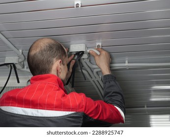 an electrician works, connects the wiring on the ceiling, twists the insulation. A professional employee of the company - Powered by Shutterstock