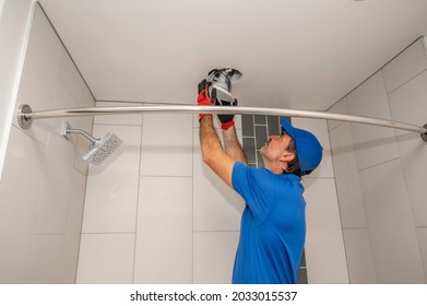 An electrician works on a light fixture on the ceiling of a bathroom