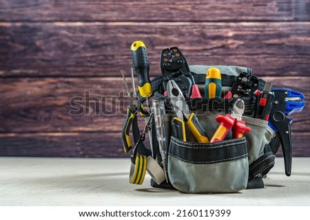 Electrician's bag with a professional electric tools. Pliers, wire cutters, strippers, screwdrivers, testers, crimping pliers. Dark wood background. Front view. Place fot text. Stock fotó © 