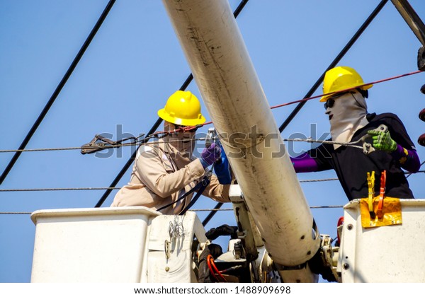 Electricians working on cable car to repair\
the power line under light blue sky\
background.