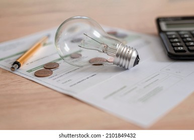 Electricity bill with light bulb, several coins, calculator and pen on the desk. Concept of electricity prices and tax payments. - Shutterstock ID 2101849432