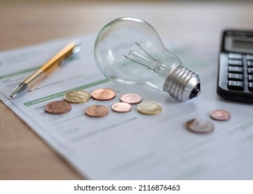 Electricity bill with light bulb, several coins, calculator and pen on the desk. Concept of electricity prices and tax payments. - Shutterstock ID 2116876463