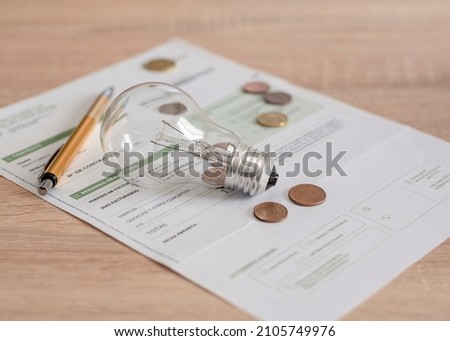 Electricity bill with light bulb, several coins and pen on the desk. Concept of electricity prices and tax payments.