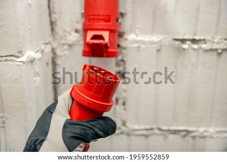 Electricity cost, electricity price, high voltage industrial socket. High voltage plug in hand. Connecting a 380 volt high voltage, three phase plug to an outlet.