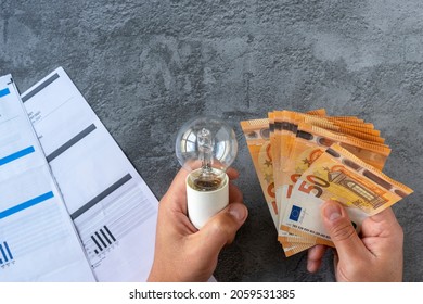 Electricity costs: Person checking electricity bills with a light bulb in one hand and several euro bills in the other hand. Concept saving electricity costs. High quality photo