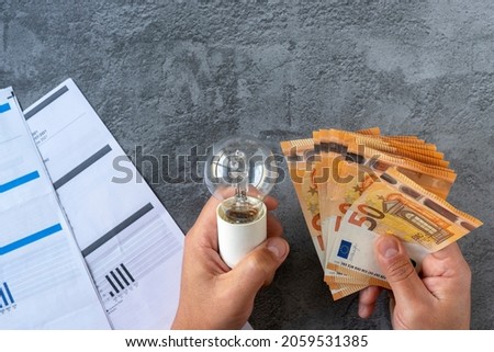 Electricity costs: Person checking electricity bills with a light bulb in one hand and several euro bills in the other hand. Concept saving electricity costs. High quality photo