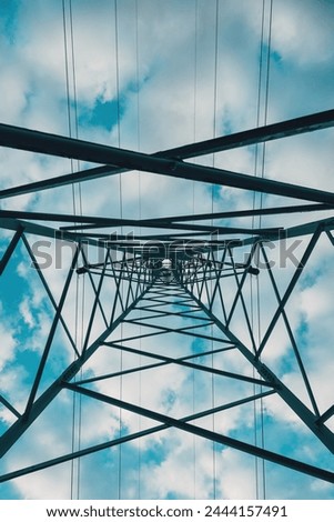 Electricity distribution tower from below, high voltage power lines under cloudy sky. Low angle view.