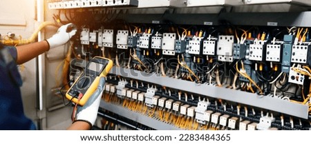 Electricity or electrical maintenance service, Electrician hand holding measuring meter checking electric current voltage circuit breaker cable wiring check main power load center distribution board.