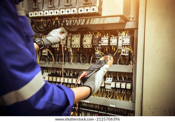 Electricity and electrical maintenance service,\
Engineer using measuring equipment tool checking electric current\
voltage at circuit breaker terminal and cable wiring main power\
distribution board.