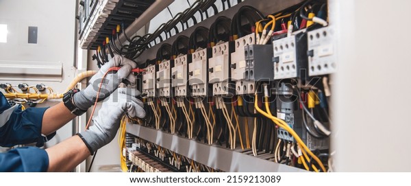 Electricity and electrical maintenance service,\
Engineer hand holding AC voltmeter checking electric current\
voltage at circuit breaker terminal and cable wiring main power\
distribution board.
