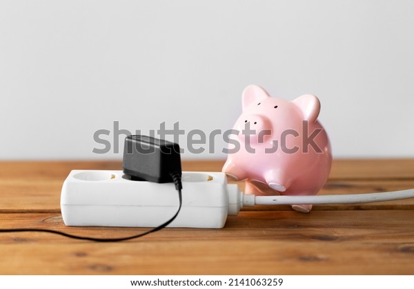 electricity, energy crisis and\
power consumption concept - close up of piggy bank and electric\
socket