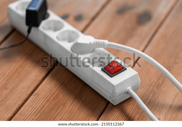 electricity, energy and power consumption concept -\
close up of socket with plugs, charger and red switch button on\
wooden floor
