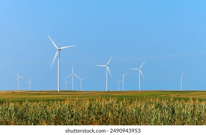 Electricity generating station. Alternative Energy Windmill Farm. Wind turbines standing tall in a field of corn under a clear blue sky, showcasing renewable energy and sustainable agriculture. - Powered by Shutterstock