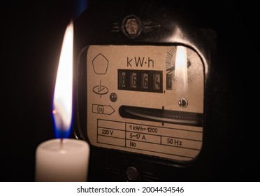 Electricity Meter Illuminated By The Light Of A Burning Candle. Power Outage Or Blackout Concept Image.