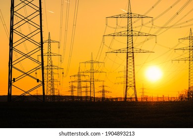 Electricity poles and electric power transmission lines against vibrant orange sky at sunset on a hot day with flickering air. High Voltage towers provide power supply over a long distance. - Powered by Shutterstock