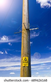 Electricity Poles Reach Up Into The Deep Blue Sky. A Warning Sign Warns Of Impending Danger