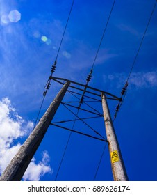 Electricity Poles Reach Up Into The Deep Blue Sky. A Warning Sign Warns Of Impending Danger