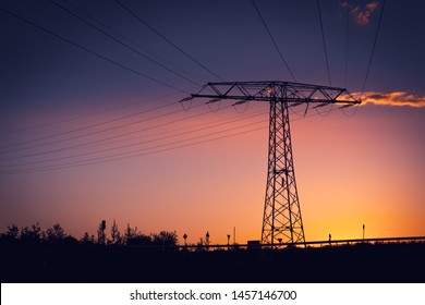 Electricity Pylon With High Voltage Power Lines Silhouetted Against A Colorful Orange And Purple Sunset With Copy Space At Twilight