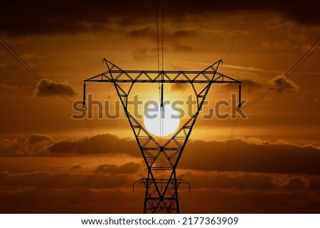 Electricity pylon or tower framing the setting sun. Green energy and electric power. Man made Cop28