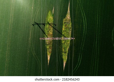 Electricity Transmission Tower And Power Line In Agricultural Field, Top View From Drone Pov On Sunny Spring Day