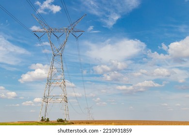 Electricity Transmission Towers In Rural Farm Field. Electrical Power Grid And Distribution Safety, Security And Maintenance Concept