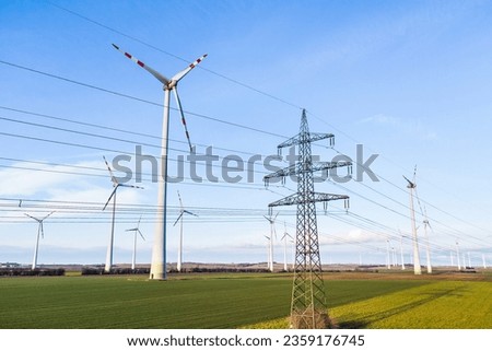 Electricyl pylon with cables on an agricultural field surrounded by windmills for wind power production