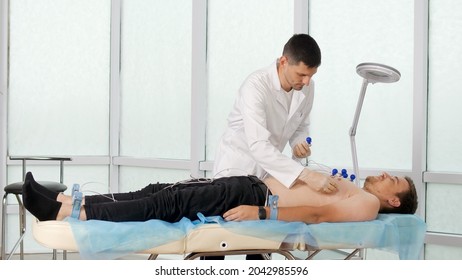 Electrocardiogram Procedure for Diagnosing Heart Disease. A Cardiologist Puts Electrodes on the Bare Chest of a Young Man Lying on the Couch To Take an Electrocardiogram in the Clinic'S Office. - Shutterstock ID 2042985596