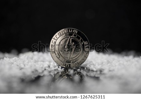 Electroneum cryptocurrency physical coin surrounded with fake snow on reflective black surface