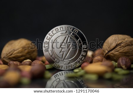 Electroneum ETN cryptocurrency physical coin surrounded with variety of nuts, including walnuts, hazelnuts, almonds and pumpkin seeds in the black background