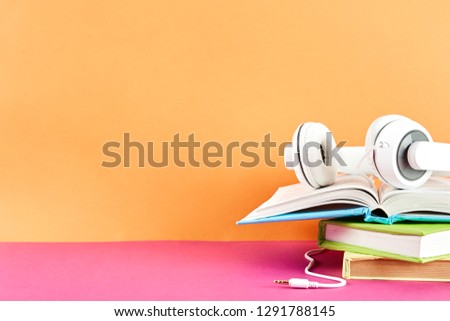 Electronic audiobook vs regular paper book concept. Stack of different color hardcover books with blank colorful covers & white headphones on table. Old versus new. Close up, copy space, background.