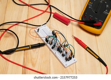 Electronic breadboard with resistor, transistor, wires and Orange digital multimeter with probes on wooden background