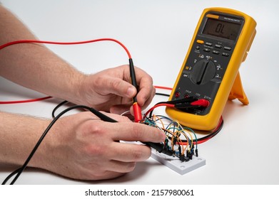 Electronic breadboard with resistor, transistor, wires and Orange digital multimeter with probes in man hands on white background