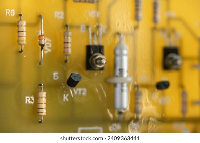Electronic circuit board made of yellow fiberglass with soldered resistors and capacitors on metal legs marked with letters and numbers. Computer circuit close-up in blur with copy space.
