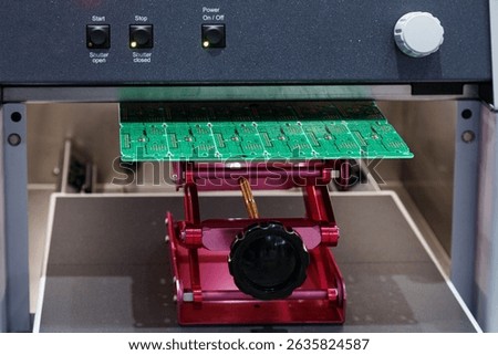 electronic circuit board under processing machine. Close-up of green PCB manufacturing stage with illuminated control panel. Electronic components production and assembly line. 