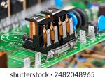 Electronic components as electromagnetic relays or glass electric fuse on green PCB. Closeup two electromechanical switches with copper wire on coil with iron core, yoke and armature on circuit board.