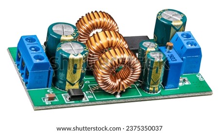 Electronic components on circuit board of power supply converter isolated on white background. Close-up of toroidal coils, electrolytic capacitors or resistor trimmer and screw terminals on green PCB.