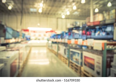 Electronic Department Store With Bokeh Blurred Background. Television Retail Shop, TVs Display On Shelf At Wholesale Store. Defocused Background Of Warehouse Interior Technology Aisle. Vintage Filter.