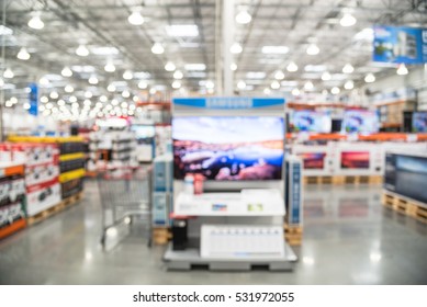 Electronic Department Store With Bokeh Blurred Background. Television Retail Shop, TVs Display On Shelf At Wholesale Store. Defocused Warehouse Interior Technology Aisle, Shelves And Shopping Cart.