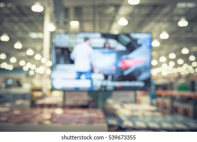 Electronic Department Store With Bokeh Blurred Background. Television Retail Shop, TVs Display On Shelf At Wholesale Store. Defocused Warehouse Interior Technology Aisle And Shelves. Vintage Tone.