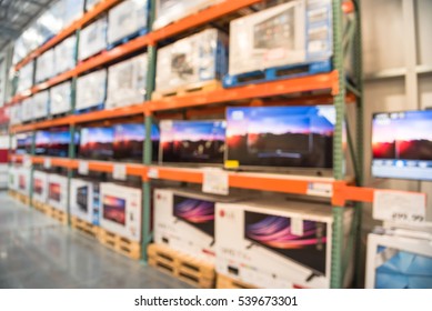 Electronic Department Store With Row Of TVs And Boxes On Shelves Display From Floor To Ceiling. Television Retail Shop, TVs Shelf Wholesale Store. Defocused Warehouse Interior Technology Aisle.