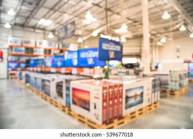 Electronic Department Store With Row Of TVs On Shelves Display. Television Retail Shop, TVs Shelf Wholesale Store. Defocused Warehouse Interior Technology Aisle, Inventory, Export, Business Concept.